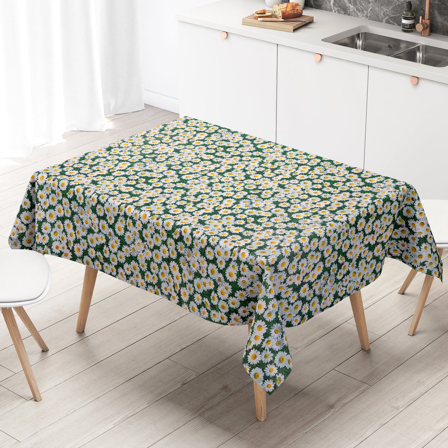 Rechteckige Wachstuch-Tischdecke mit dichtem Gänseblümchen-Muster. Zahlreiche weiße Blüten mit gelber Mitte bedecken einen grünen Hintergrund aus Blättern und Gräsern und erzeugen die Optik einer blühenden Sommerwiese. Zwischen den Blüten sind vereinzelt kleine Marienkäfer zu sehen, die dem floralen Design einen natürlichen und verspielten Akzent verleihen. Die Tischdecke fällt über die Kanten eines Tisches herab.