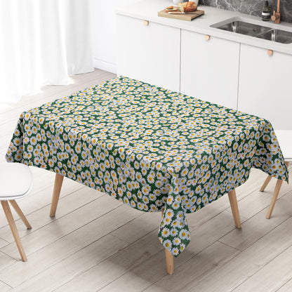 Rechteckige Wachstuch-Tischdecke mit dichtem Gänseblümchen-Muster. Zahlreiche weiße Blüten mit gelber Mitte bedecken einen grünen Hintergrund aus Blättern und Gräsern und erzeugen die Optik einer blühenden Sommerwiese. Zwischen den Blüten sind vereinzelt kleine Marienkäfer zu sehen, die dem floralen Design einen natürlichen und verspielten Akzent verleihen. Die Tischdecke fällt über die Kanten eines Tisches herab.