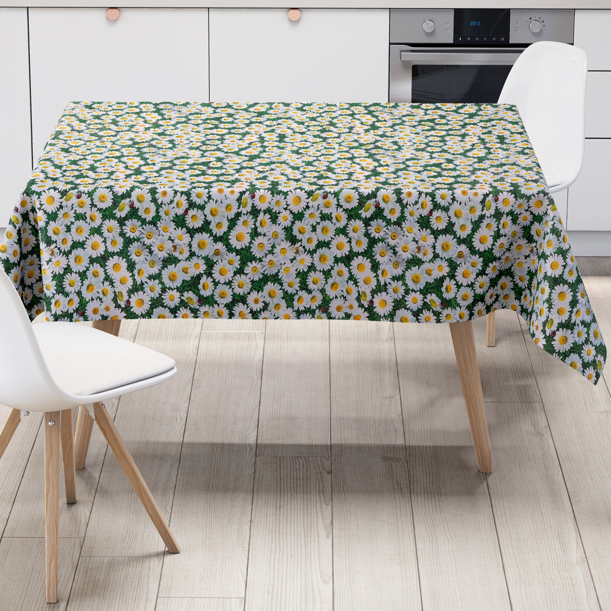 Rechteckige Wachstuch-Tischdecke mit dichtem Gänseblümchen-Muster. Zahlreiche weiße Blüten mit gelber Mitte bedecken einen grünen Hintergrund aus Blättern und Gräsern und erzeugen die Optik einer blühenden Sommerwiese. Zwischen den Blüten sind vereinzelt kleine Marienkäfer zu sehen, die dem floralen Design einen natürlichen und verspielten Akzent verleihen. Die Tischdecke fällt über die Kanten eines Tisches herab.