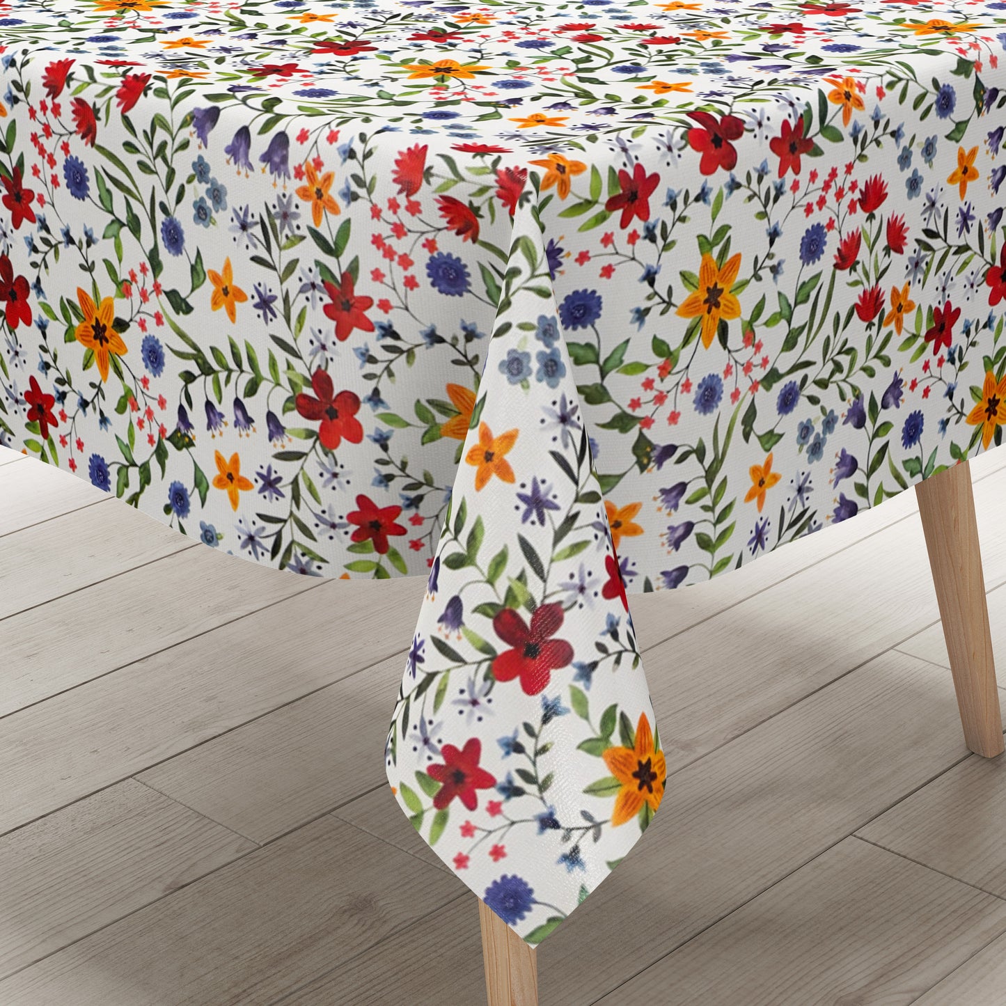 Weiße Wachstuch-Tischdecke mit dichtem, farbenfrohem Wildblumenmuster. Rote, gelbe, orangefarbene, blaue und violette Blüten sowie grüne Blätter und Ranken verteilen sich gleichmäßig über die gesamte Oberfläche und erinnern an eine blühende Sommerwiese im Landhausstil. Die rechteckige Tischdecke ist dekorativ über einen Tisch drapiert.