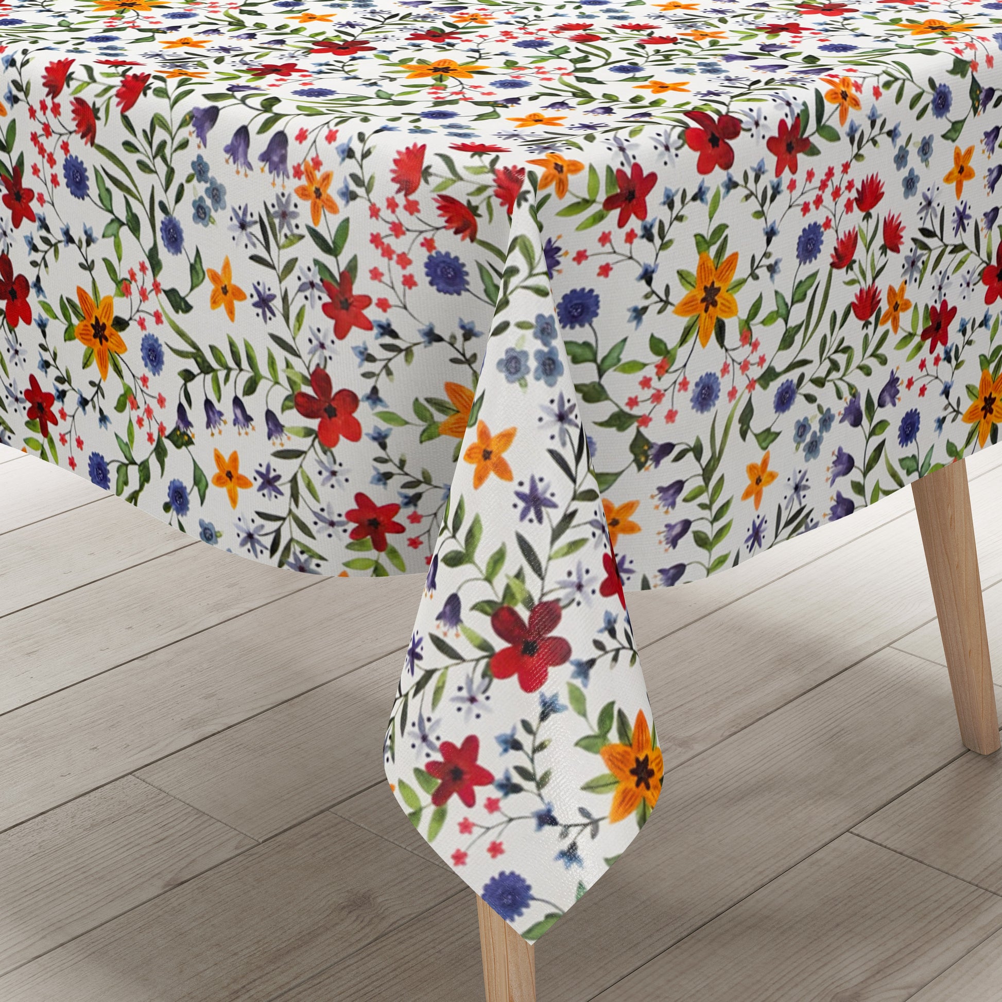 Weiße Wachstuch-Tischdecke mit dichtem, farbenfrohem Wildblumenmuster. Rote, gelbe, orangefarbene, blaue und violette Blüten sowie grüne Blätter und Ranken verteilen sich gleichmäßig über die gesamte Oberfläche und erinnern an eine blühende Sommerwiese im Landhausstil. Die rechteckige Tischdecke ist dekorativ über einen Tisch drapiert.