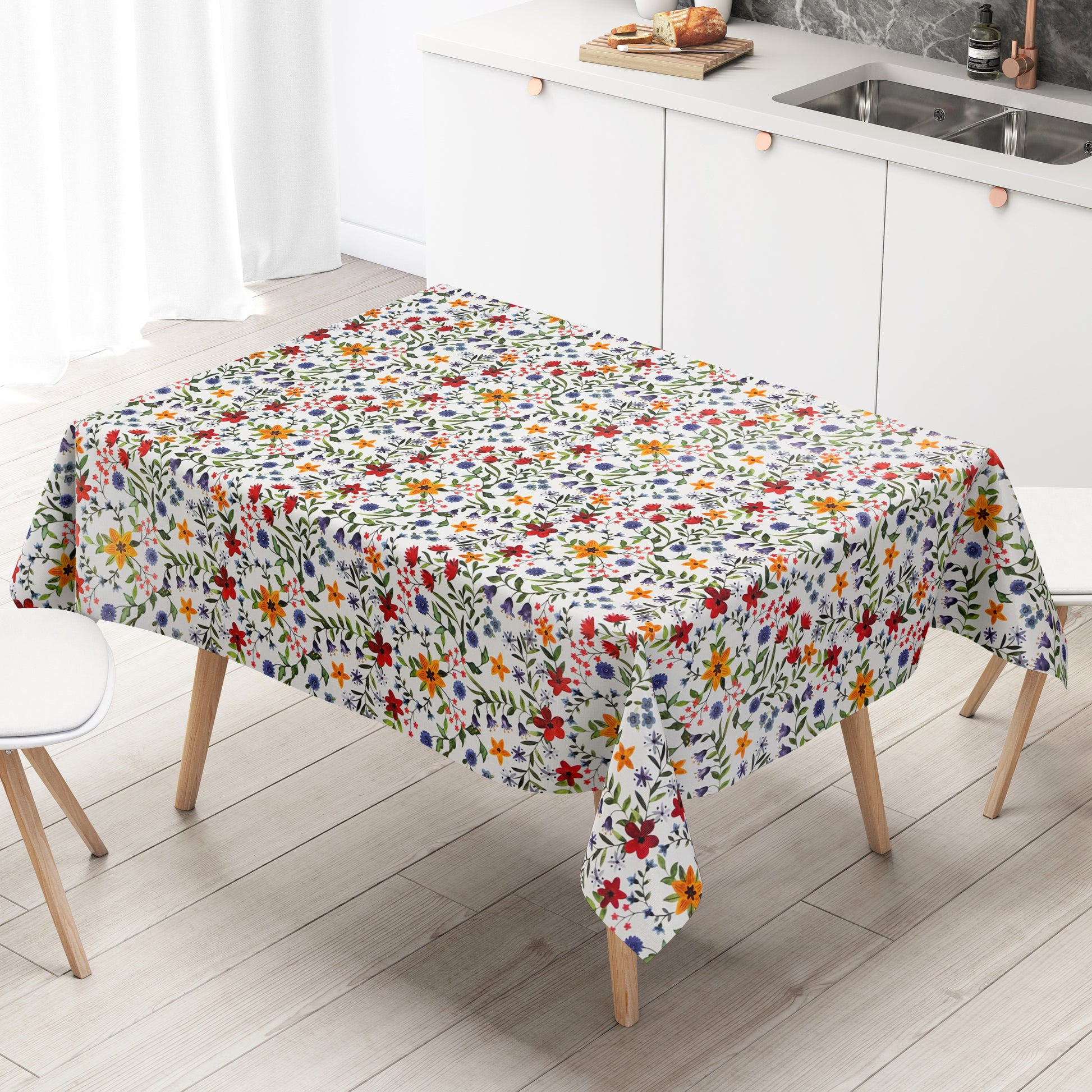 Weiße Wachstuch-Tischdecke mit dichtem, farbenfrohem Wildblumenmuster. Rote, gelbe, orangefarbene, blaue und violette Blüten sowie grüne Blätter und Ranken verteilen sich gleichmäßig über die gesamte Oberfläche und erinnern an eine blühende Sommerwiese im Landhausstil. Die rechteckige Tischdecke ist dekorativ über einen Tisch drapiert.