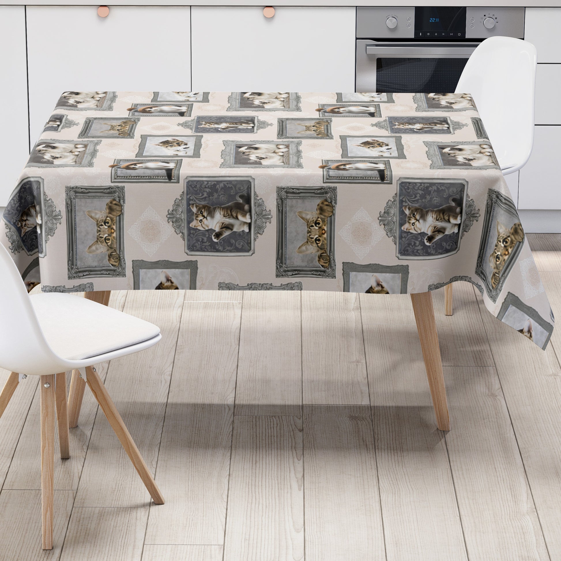 Wachstuch-Tischdecke mit cremefarbenem Hintergrund und dekorativem Katzenmotiv im Vintage-Stil. Verschiedene Katzenporträts in grauen und silbernen Bilderrahmen sind gleichmäßig über die Tischdecke verteilt. Das Design zeigt flauschige Kätzchen und neugierige Katzen mit dezenten Ornamentmustern zwischen den Rahmen.