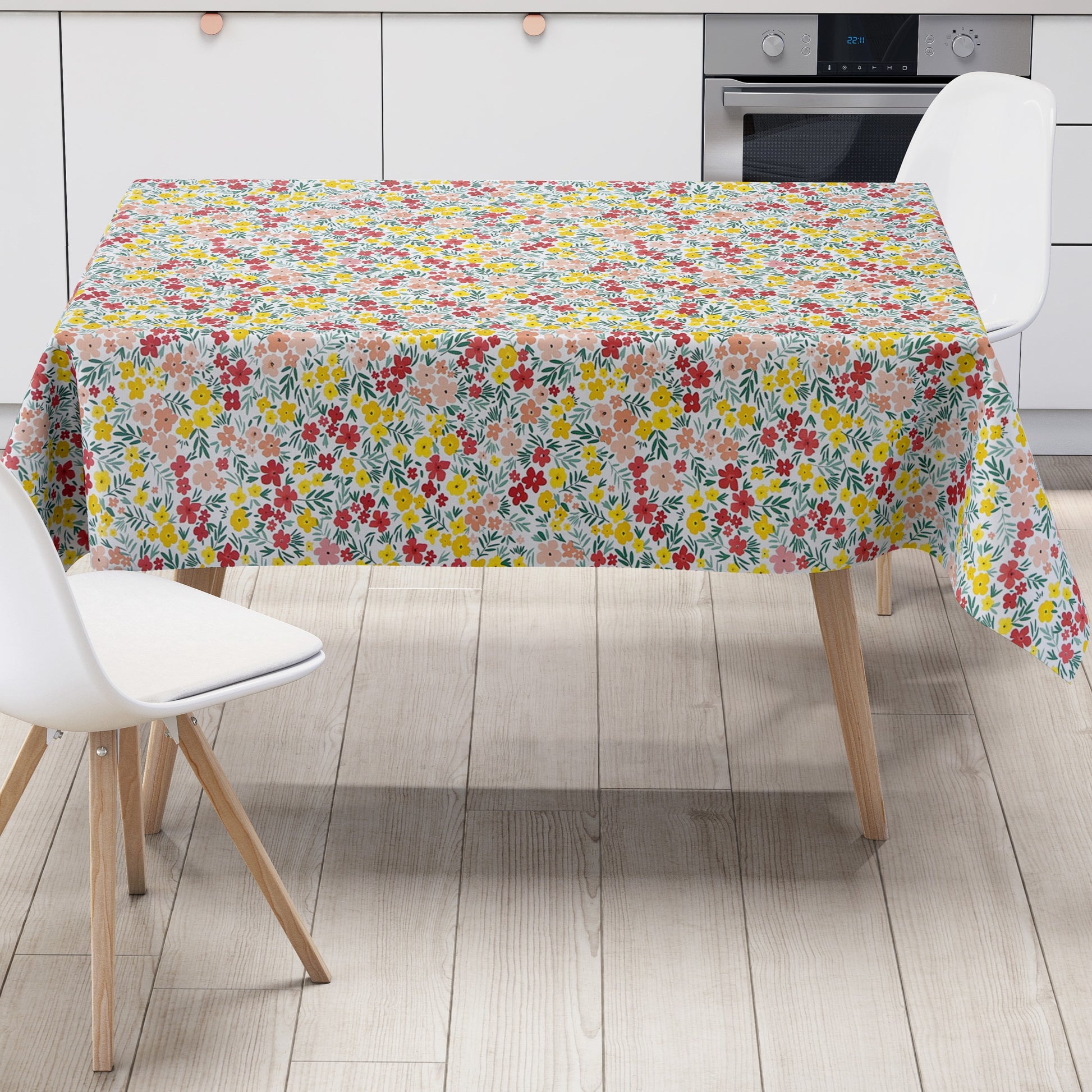 Bunte Wachstuch-Tischdecke mit dichtem Streublumenmuster in Rot, Gelb und Rosa sowie grünen Blättern auf hellem Hintergrund, über eine rechteckige Tischkante drapiert.