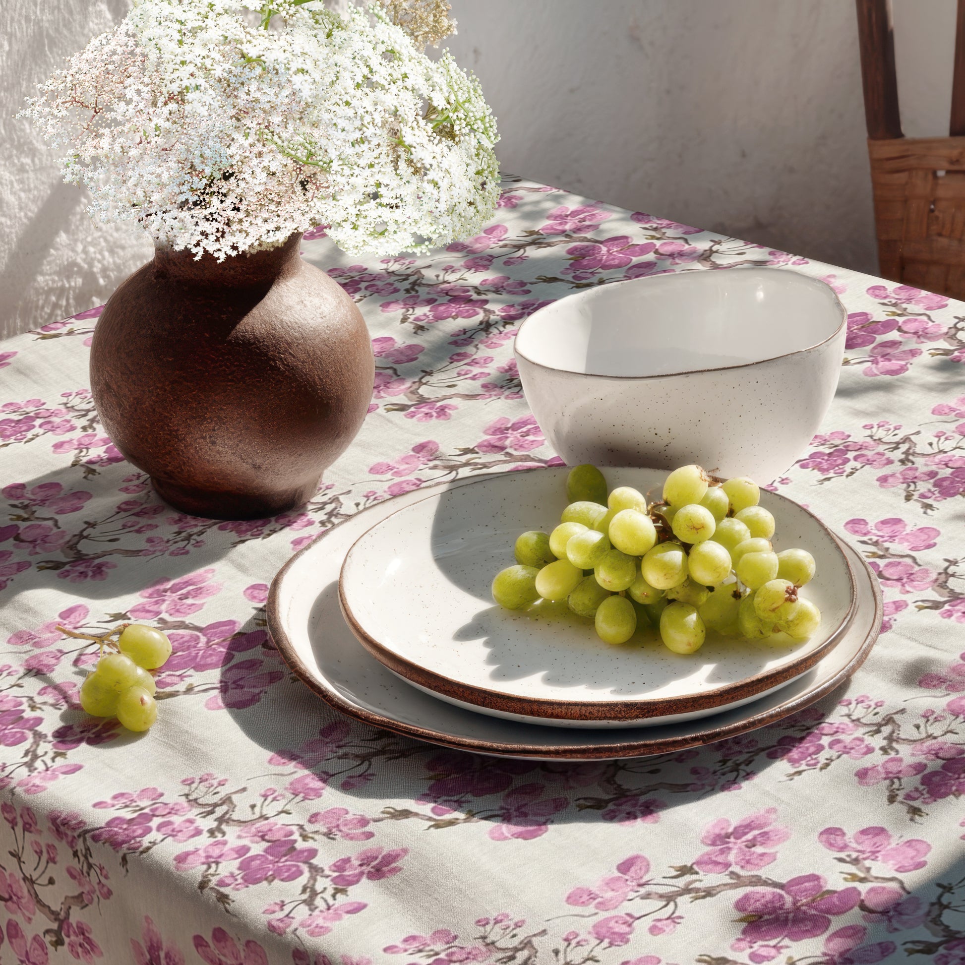 Beschichtete Jacquard-Tischdecke aus Baumwolle mit Fleckenschutz im Design JQ1425, weißer Hintergrund mit einem floralen Allover-Muster aus rosafarbenen Kirschblüten auf filigranen braunen Zweigen.