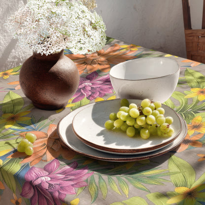 Beschichtete Jacquard-Tischdecke aus Baumwolle mit Fleckenschutz im Design JQ1426, taupefarbener Hintergrund mit tropischem Allover-Muster aus großen Lilien, exotischen Blüten und grünen Palmblättern in Orange, Violett, Gelb und Grün.