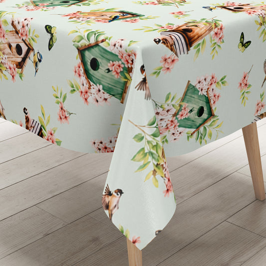 Wachstuch-Tischdecke mit Vogelhäuschen, kleinen Vögeln, Schmetterlingen und rosa Blüten auf hellem mintfarbenem Hintergrund. Grüne Blätter und natürliche Holztöne verleihen dem verspielten Frühlingsdesign eine frische, freundliche Ausstrahlung.