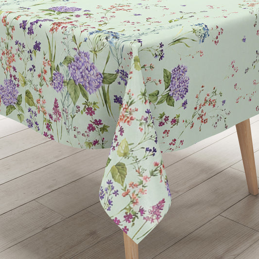 Wachstuchtischdecke mit romantischem Blumenmuster auf mintgrünem Hintergrund. Zarte Wildblumen, filigrane Zweige und Blütenranken in Rosa, Blau, Lila und Rot verteilen sich locker über die Fläche. Große violette Hortensien setzen dekorative Akzente entlang der oberen und unteren Bereiche. Das detailreiche, aquarellartige Dessin wirkt leicht, natürlich und verspielt und verleiht dem Tisch eine frische, florale Ausstrahlung.