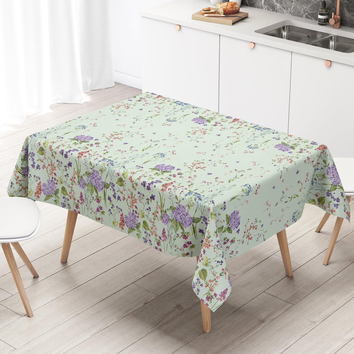 Wachstuchtischdecke mit romantischem Blumenmuster auf mintgrünem Hintergrund. Zarte Wildblumen, filigrane Zweige und Blütenranken in Rosa, Blau, Lila und Rot verteilen sich locker über die Fläche. Große violette Hortensien setzen dekorative Akzente entlang der oberen und unteren Bereiche. Das detailreiche, aquarellartige Dessin wirkt leicht, natürlich und verspielt und verleiht dem Tisch eine frische, florale Ausstrahlung.