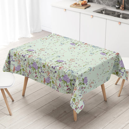 Wachstuchtischdecke mit romantischem Blumenmuster auf mintgrünem Hintergrund. Zarte Wildblumen, filigrane Zweige und Blütenranken in Rosa, Blau, Lila und Rot verteilen sich locker über die Fläche. Große violette Hortensien setzen dekorative Akzente entlang der oberen und unteren Bereiche. Das detailreiche, aquarellartige Dessin wirkt leicht, natürlich und verspielt und verleiht dem Tisch eine frische, florale Ausstrahlung.
