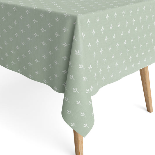 Salbeigrüne Tischdecke aus beschichteter Baumwolle mit Fleckenschutz und kleinen weißen Blattmustern, dekorativ über einem Tisch drapiert.