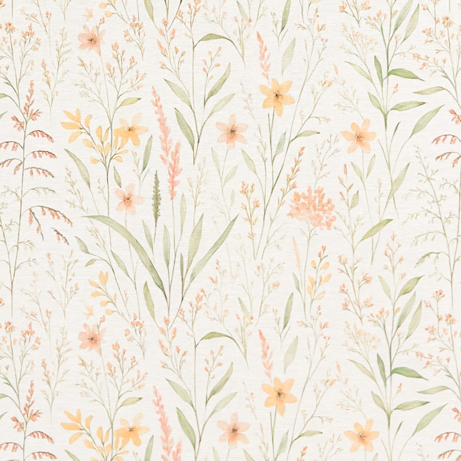 Beschichtete Baumwoll-Tischdecke mit filigranem Naturmuster auf hellem Hintergrund. Zarte Gräser, Blätter und kleine Blüten in Apricot-, Gelb- und Grüntönen verteilen sich gleichmäßig über die Oberfläche. Über eine Tischecke drapiert, mit sichtbaren hellen Holzbeinen.