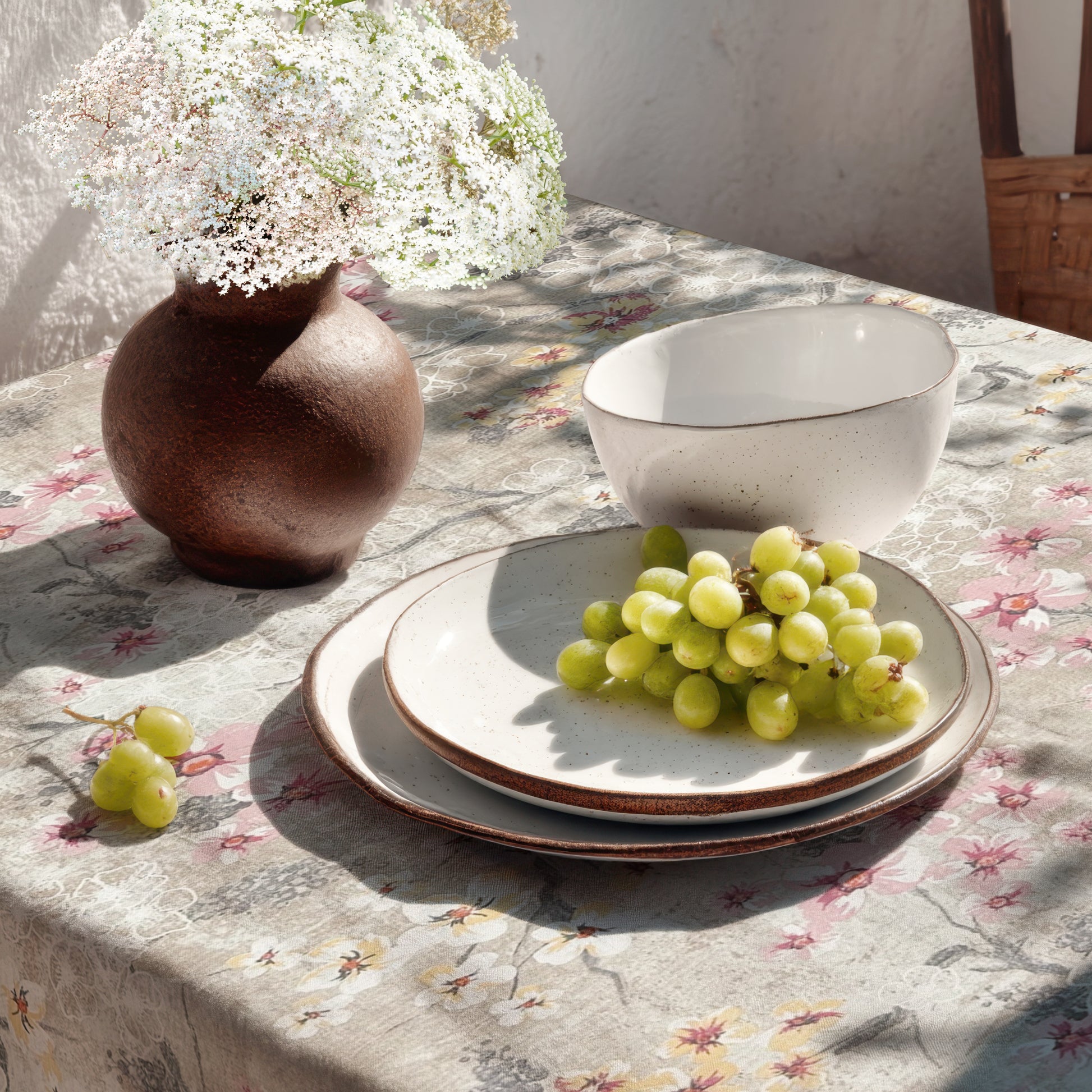 Beschichtete Baumwoll-Tischdecke mit Fleckenschutz im Design ROVIERA, naturfarbener Hintergrund mit zarten Kirschblüten in Weiß, Rosa und Creme auf filigranen Zweigen sowie dekorativen floralen Konturen in Beige- und Grautönen.