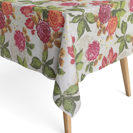 Beschichtete Baumwoll-Tischdecke mit großem floralem Muster auf hellem Hintergrund. Auffällige Blüten in Pink, Rot und Orange sowie grüne Blätter verteilen sich über die Oberfläche. Über eine Tischecke drapiert, mit sichtbaren hellen Holzbeinen.